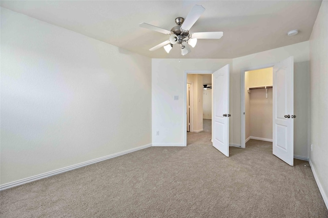 unfurnished bedroom with a walk in closet, ceiling fan, a closet, and light carpet