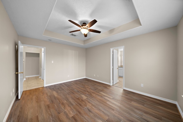 unfurnished bedroom with dark hardwood / wood-style floors, ceiling fan, a textured ceiling, a tray ceiling, and a closet