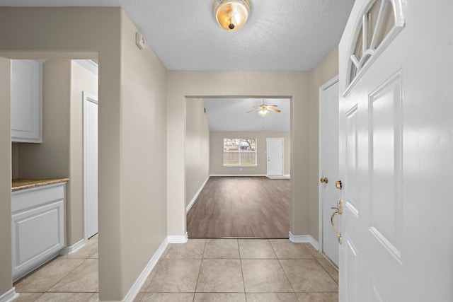 hallway featuring a textured ceiling, light hardwood / wood-style flooring, and vaulted ceiling