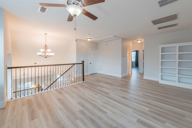 empty room with built in shelves, light wood-type flooring, and ceiling fan with notable chandelier