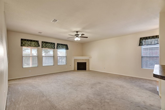 unfurnished living room with ceiling fan, a fireplace, light colored carpet, and a healthy amount of sunlight