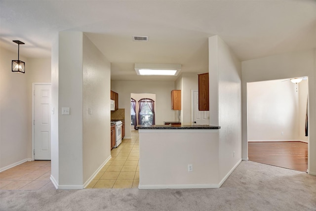 kitchen featuring kitchen peninsula, white appliances, light colored carpet, and hanging light fixtures