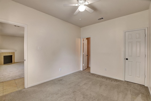 unfurnished bedroom featuring a tiled fireplace, ceiling fan, and light carpet