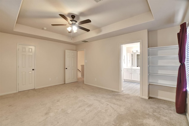 unfurnished bedroom with a tray ceiling, ceiling fan, light colored carpet, and ensuite bathroom