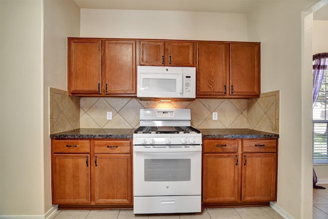 kitchen featuring decorative backsplash, light tile patterned flooring, dark stone counters, and white appliances