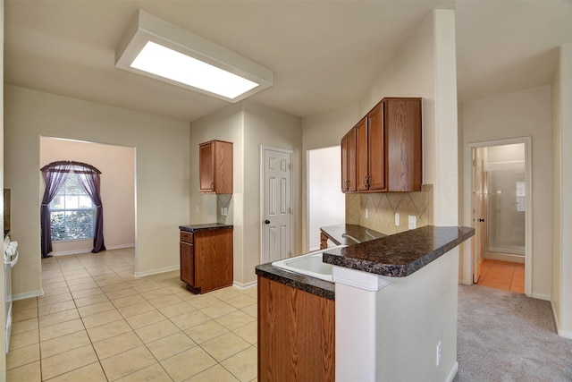 kitchen with kitchen peninsula, backsplash, light tile patterned flooring, and sink