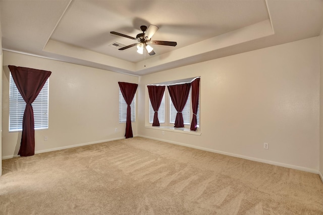 carpeted empty room with a raised ceiling and ceiling fan