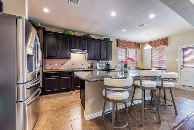 kitchen with a breakfast bar area, stainless steel fridge with ice dispenser, a kitchen island with sink, and decorative light fixtures