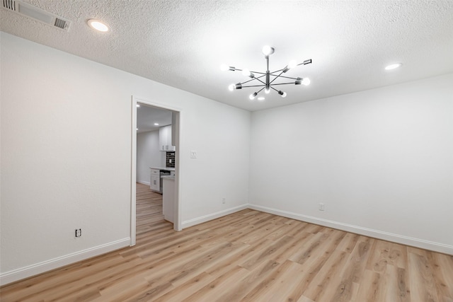 unfurnished room featuring a chandelier, a textured ceiling, and light hardwood / wood-style flooring