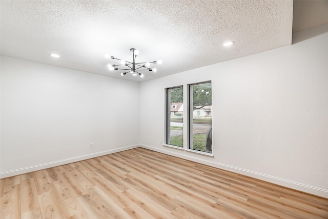 spare room featuring a textured ceiling, light hardwood / wood-style floors, and a notable chandelier