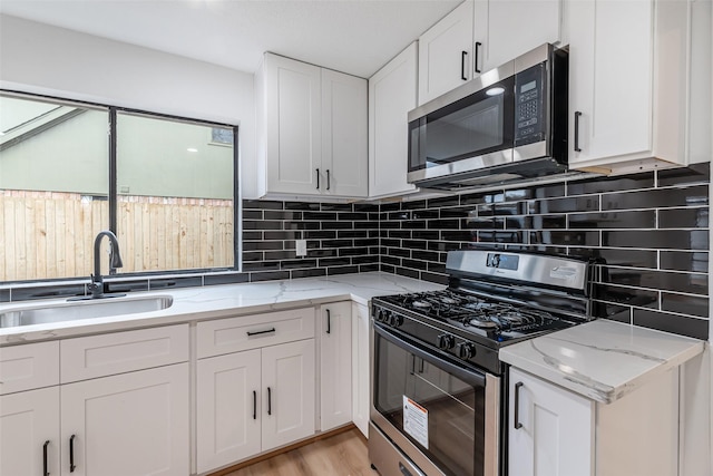 kitchen with decorative backsplash, appliances with stainless steel finishes, light stone counters, sink, and white cabinets