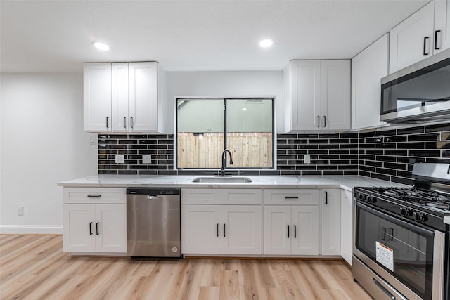 kitchen featuring light stone countertops, white cabinetry, sink, light hardwood / wood-style flooring, and appliances with stainless steel finishes