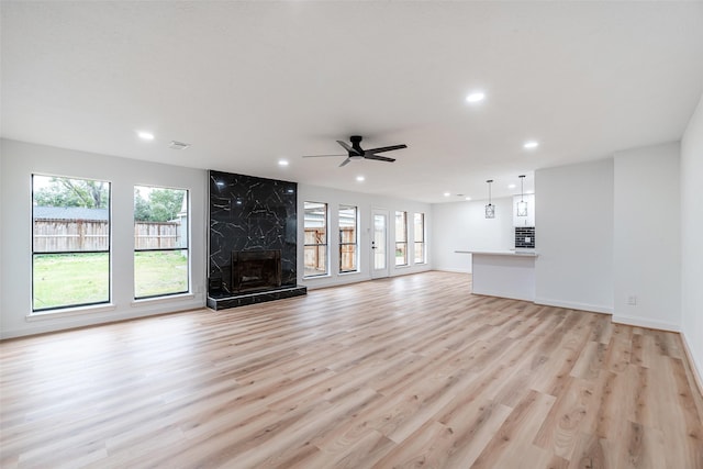 unfurnished living room featuring ceiling fan, light hardwood / wood-style flooring, a high end fireplace, and a healthy amount of sunlight