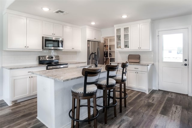 kitchen featuring a center island with sink, a kitchen breakfast bar, appliances with stainless steel finishes, dark hardwood / wood-style flooring, and white cabinetry