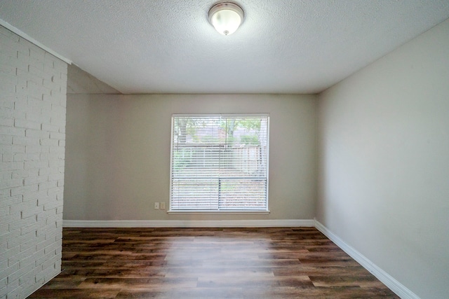 spare room with dark hardwood / wood-style floors, a textured ceiling, and brick wall