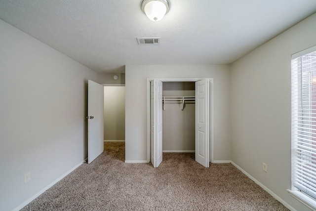 unfurnished bedroom featuring a textured ceiling, light carpet, and a closet