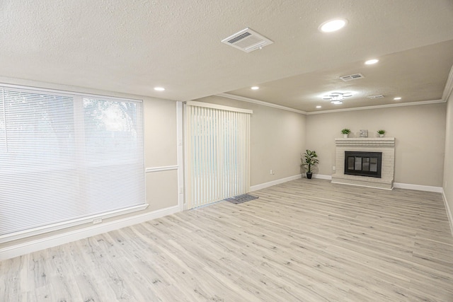 basement featuring a brick fireplace, crown molding, a textured ceiling, and light hardwood / wood-style flooring