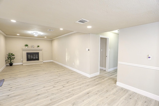 unfurnished living room featuring a fireplace, a textured ceiling, light hardwood / wood-style floors, and ornamental molding