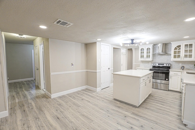 kitchen with a kitchen island, stainless steel electric stove, wall chimney range hood, light hardwood / wood-style flooring, and white cabinetry