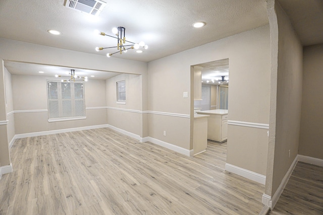 unfurnished room featuring an inviting chandelier, a textured ceiling, and light wood-type flooring