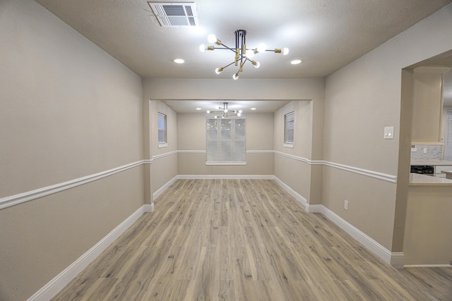 unfurnished dining area with light hardwood / wood-style flooring, a textured ceiling, and an inviting chandelier