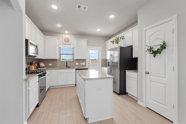 kitchen featuring appliances with stainless steel finishes, sink, white cabinets, light hardwood / wood-style floors, and a kitchen island