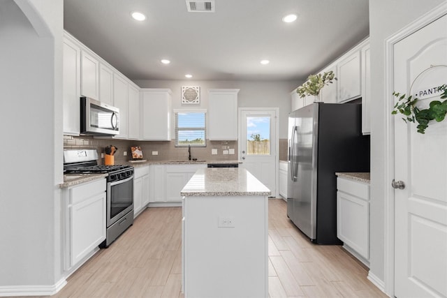 kitchen with a center island, decorative backsplash, light stone countertops, white cabinetry, and stainless steel appliances