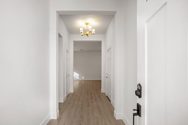 corridor with light hardwood / wood-style flooring and a notable chandelier