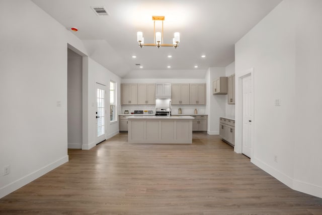 kitchen with hardwood / wood-style floors, hanging light fixtures, vaulted ceiling, a kitchen island, and stainless steel range oven