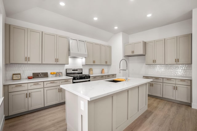 kitchen with stainless steel gas stove, light hardwood / wood-style flooring, sink, and an island with sink