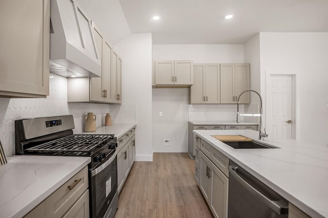 kitchen with sink, light stone counters, appliances with stainless steel finishes, custom range hood, and light wood-type flooring