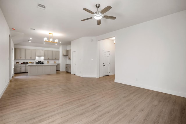 unfurnished living room featuring ceiling fan with notable chandelier and light hardwood / wood-style floors