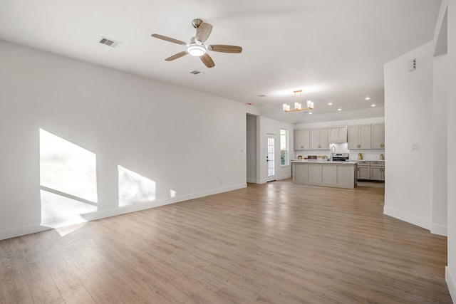 unfurnished living room featuring ceiling fan with notable chandelier, light hardwood / wood-style floors, and sink