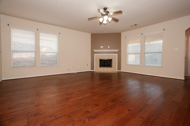 unfurnished living room with a tile fireplace, ceiling fan, and dark wood-type flooring