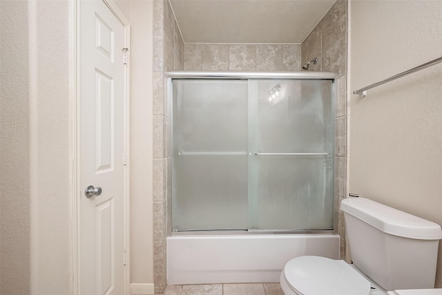 bathroom featuring tile patterned flooring, combined bath / shower with glass door, and toilet