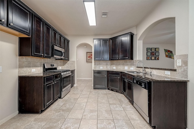 kitchen with decorative backsplash, stainless steel appliances, dark stone counters, and sink