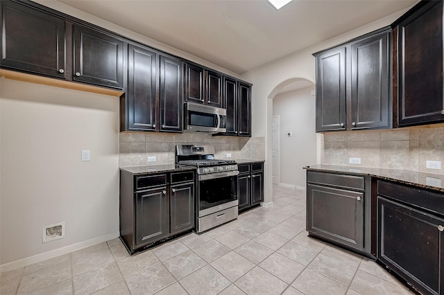 kitchen featuring decorative backsplash, light tile patterned floors, dark stone counters, and appliances with stainless steel finishes