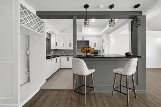 kitchen featuring hanging light fixtures, dark hardwood / wood-style floors, tasteful backsplash, white cabinets, and a kitchen bar