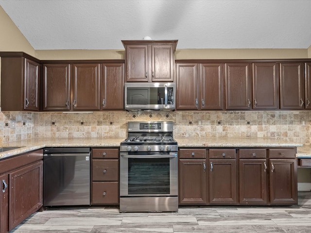 kitchen with light stone countertops, dark brown cabinetry, appliances with stainless steel finishes, and light hardwood / wood-style flooring