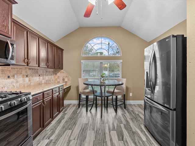 kitchen featuring light stone countertops, appliances with stainless steel finishes, backsplash, vaulted ceiling, and light hardwood / wood-style flooring