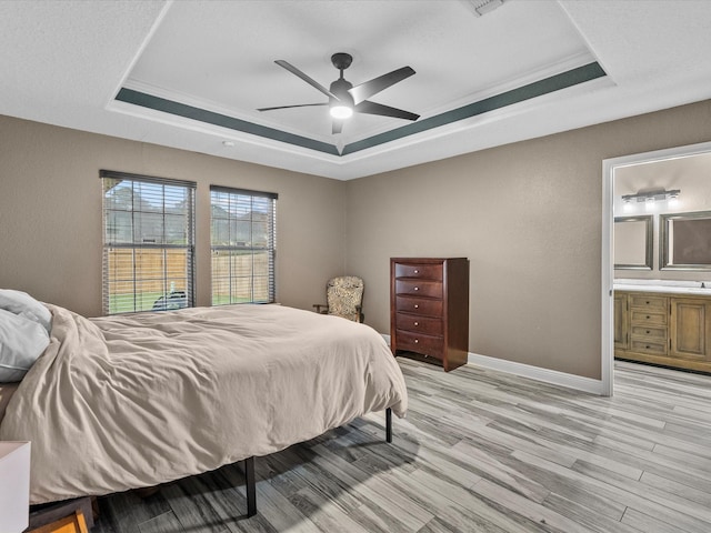 bedroom with light wood-type flooring, ornamental molding, a raised ceiling, ceiling fan, and connected bathroom