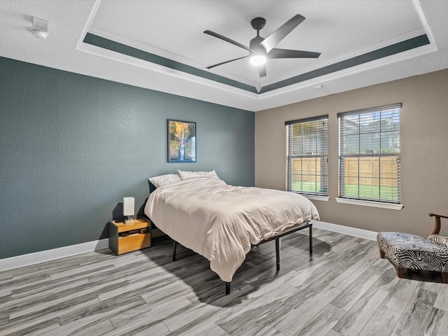 bedroom featuring ornamental molding, a tray ceiling, ceiling fan, and light hardwood / wood-style floors