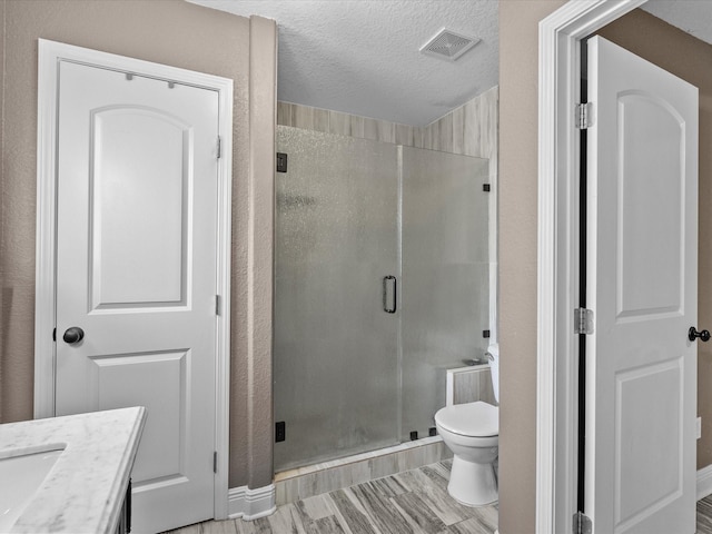 bathroom with vanity, a textured ceiling, toilet, and a shower with door