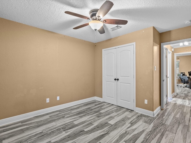 unfurnished bedroom with ceiling fan, a closet, light hardwood / wood-style floors, and a textured ceiling