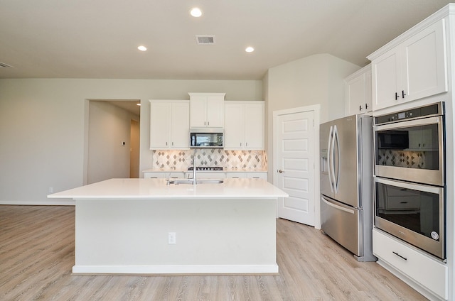 kitchen with white cabinetry, stainless steel appliances, backsplash, light hardwood / wood-style floors, and a center island with sink