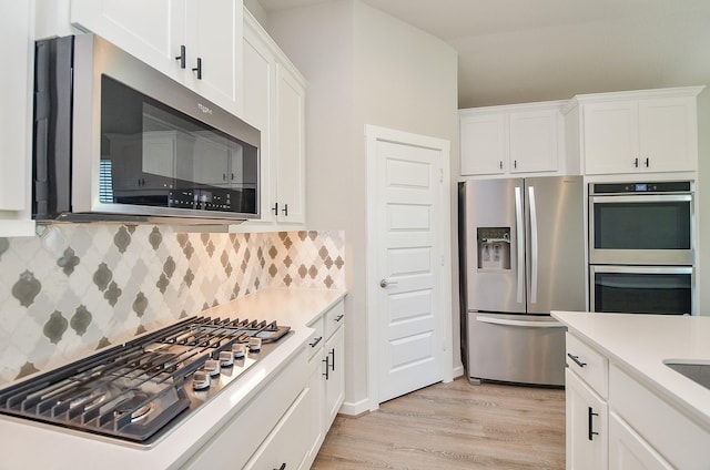 kitchen featuring backsplash, white cabinetry, stainless steel appliances, and light hardwood / wood-style flooring