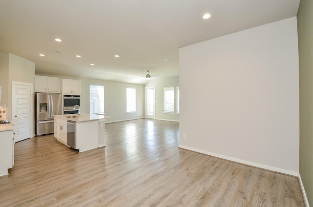 kitchen with white cabinetry, sink, an island with sink, appliances with stainless steel finishes, and light wood-type flooring