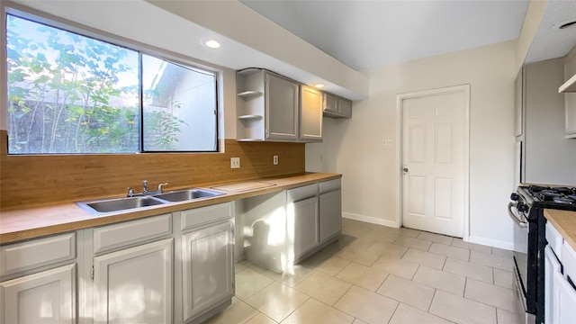 kitchen featuring wooden counters, stainless steel gas stove, gray cabinets, and sink