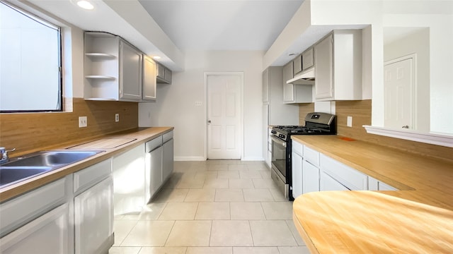 kitchen with decorative backsplash, stainless steel gas range oven, gray cabinetry, light tile patterned floors, and butcher block counters