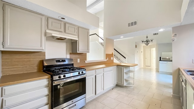 kitchen featuring a high ceiling, hanging light fixtures, light tile patterned floors, a notable chandelier, and gas stove